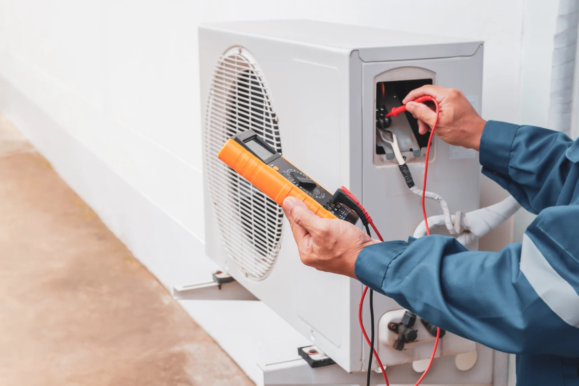 Man in a shirt holding a multimeter and checking an air conditioner, with wires connected to the device