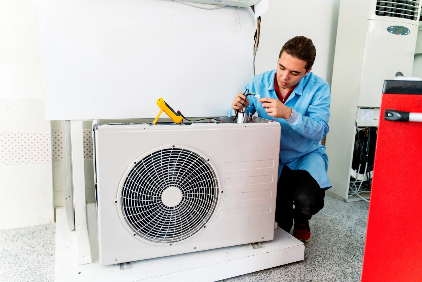 Man in a shirt working on an air conditioner in a room with a white wall in the background
