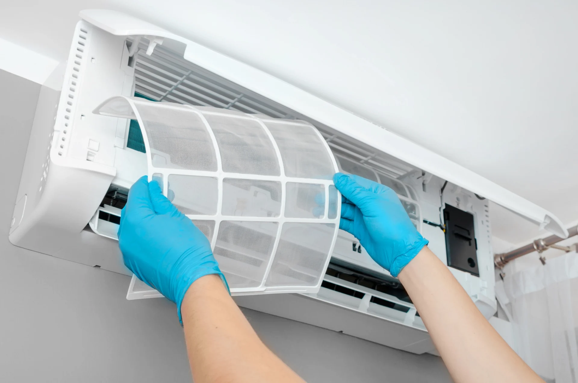 Person wearing blue gloves holding an air conditioner in their hands, with a wall in the background