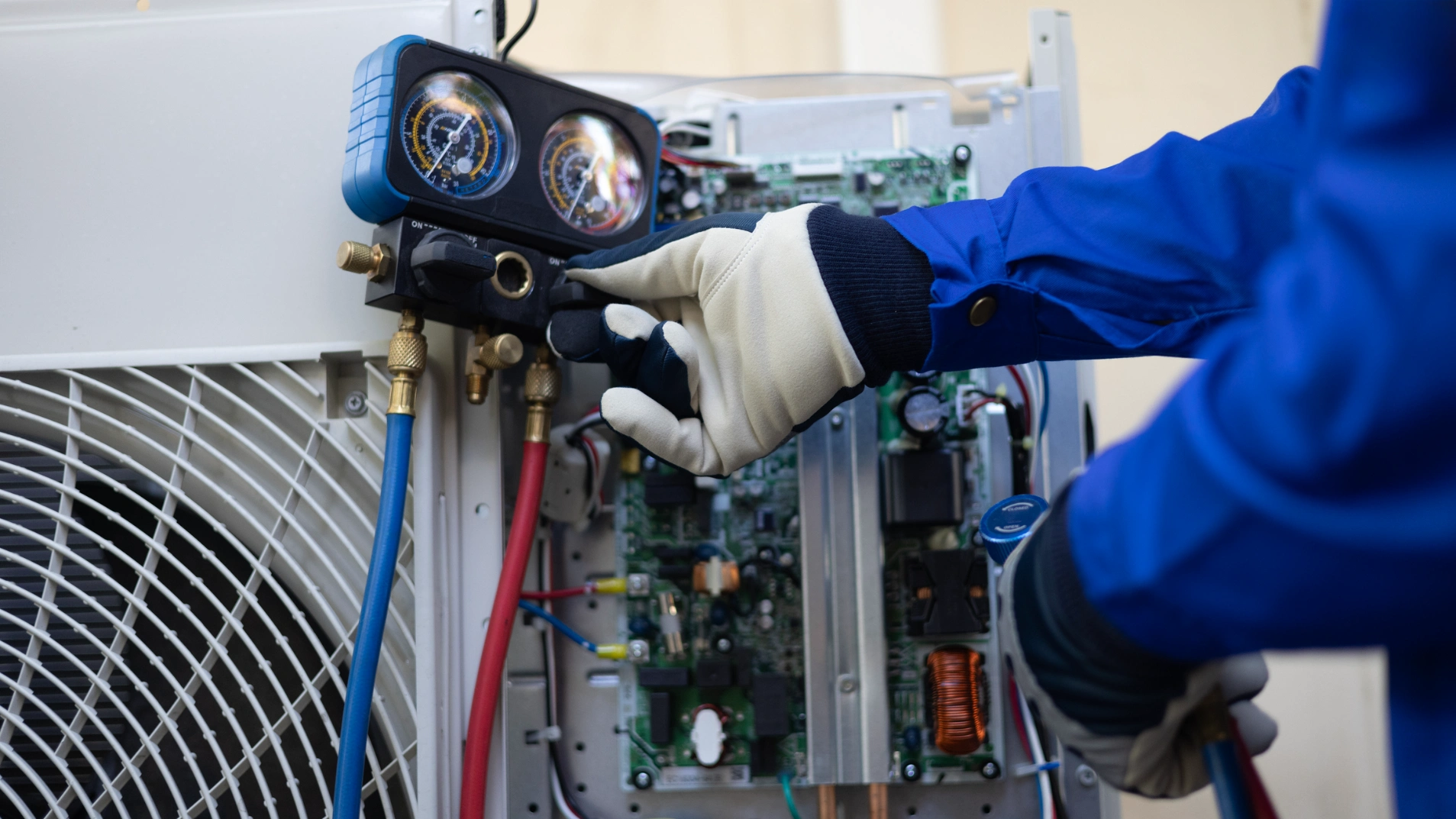 Man in a uniform working on an air conditioner, holding a meter in his hand