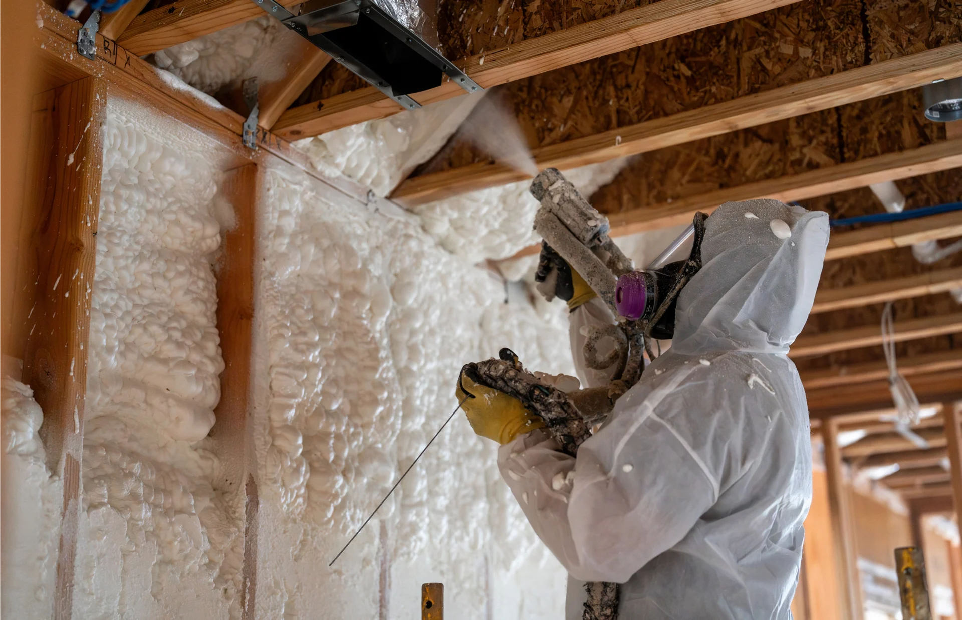 Man in a suit spraying foam insulation on a wall in a home
