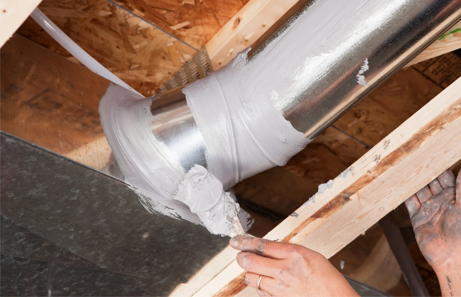 Person using a hammer to remove a piece of wood from a wooden ceiling, with a metal pipe