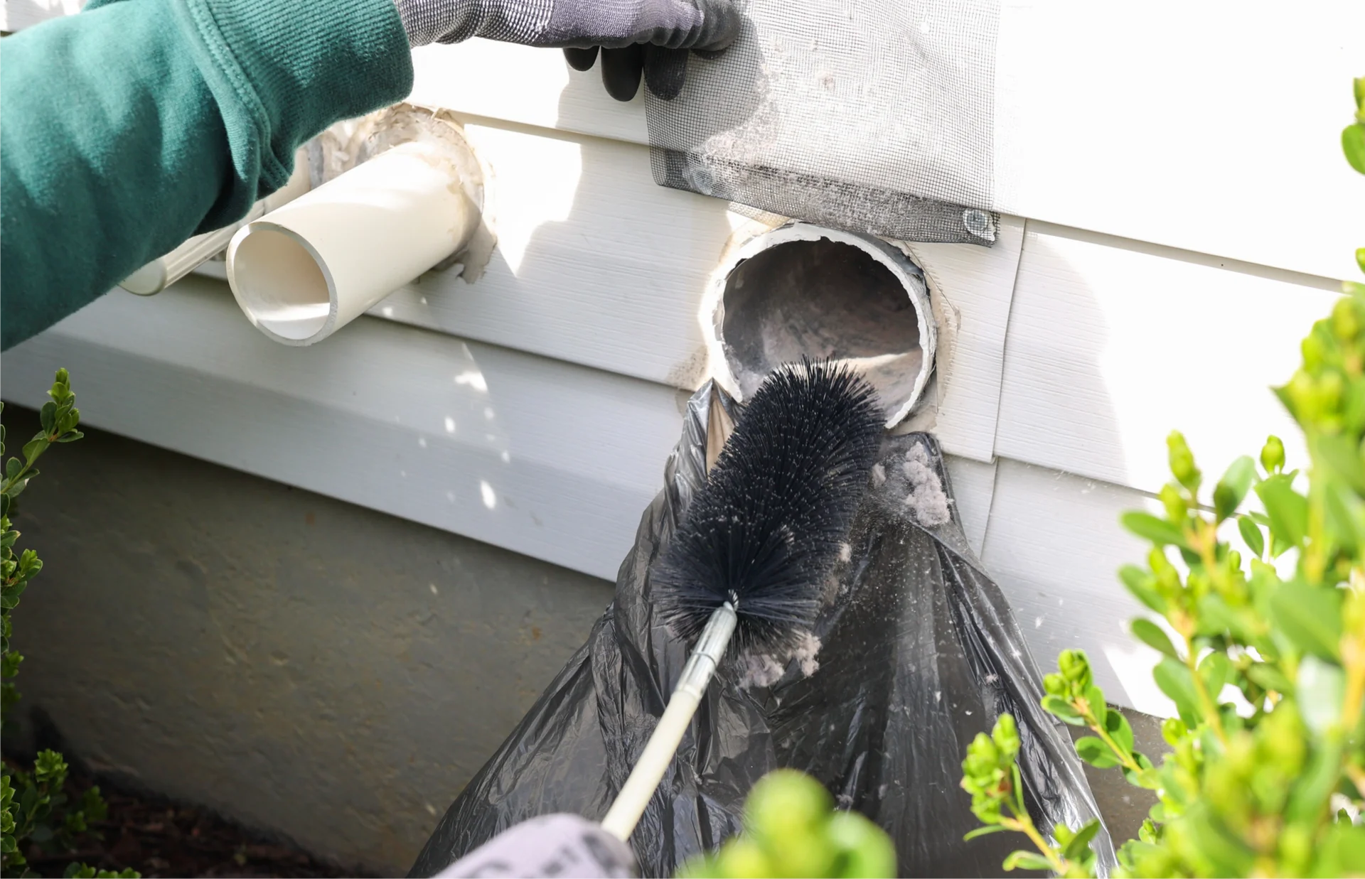 Person wearing gloves and holding a brush, cleaning a gutter with a broom