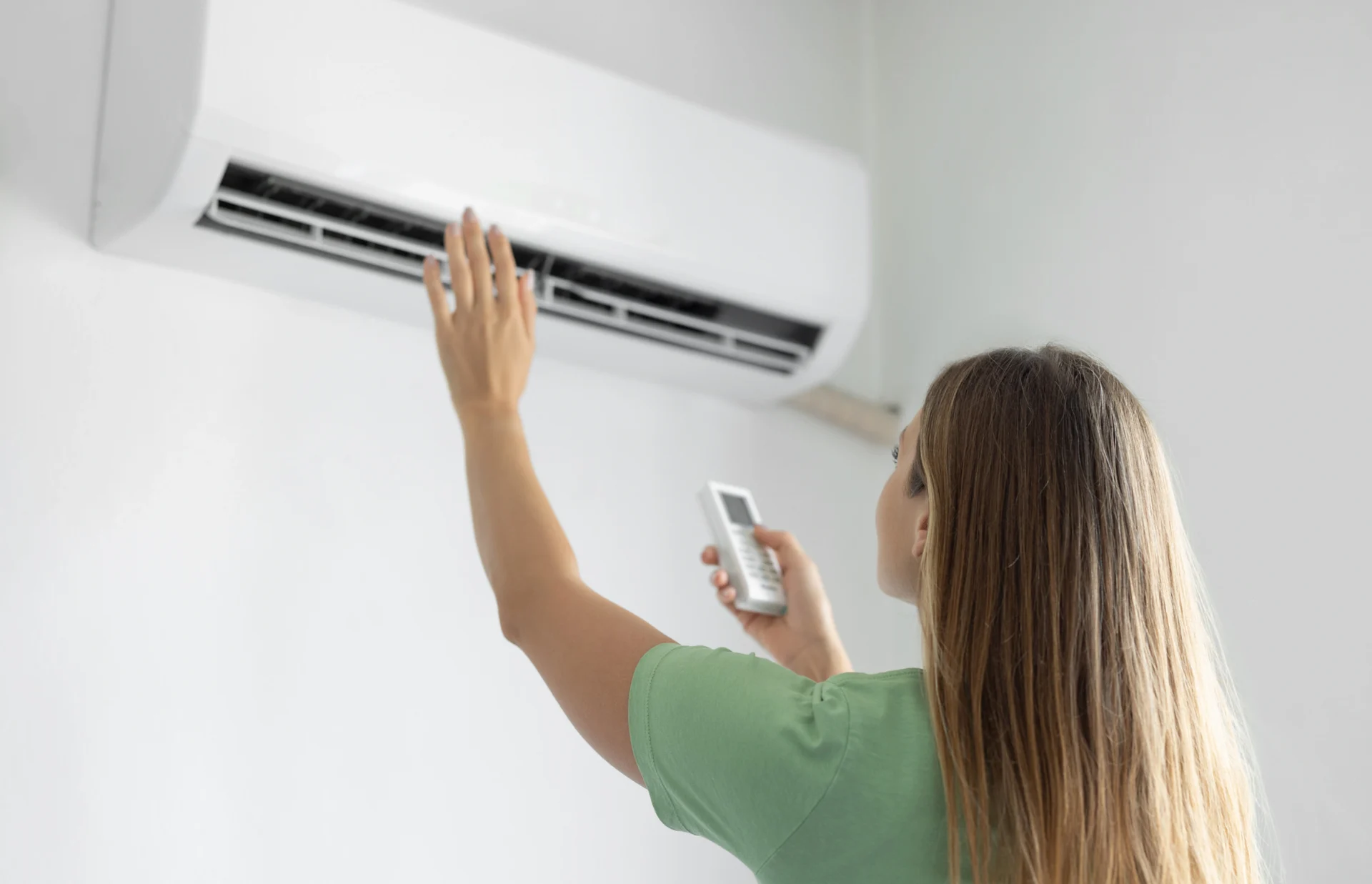 Woman in a shirt holding a remote control and adjusting an air conditioner on the wall