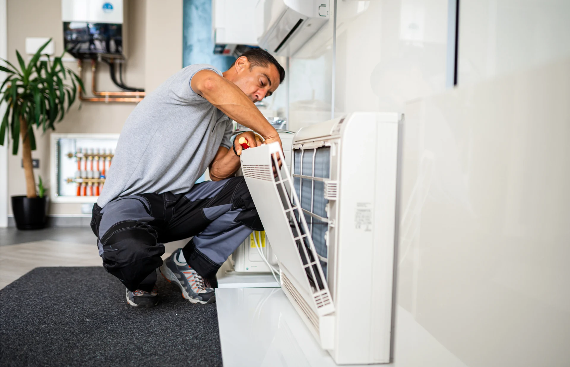 Man in a squat position on the floor, holding an object in his hand and repairing an air conditioner