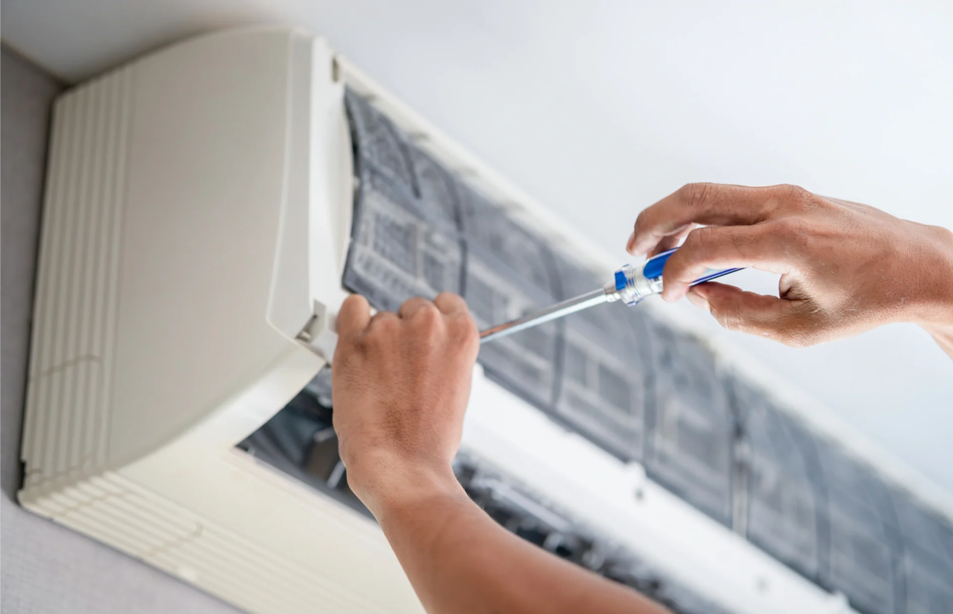 Person using a screwdriver to fix an air conditioner mounted on the wall